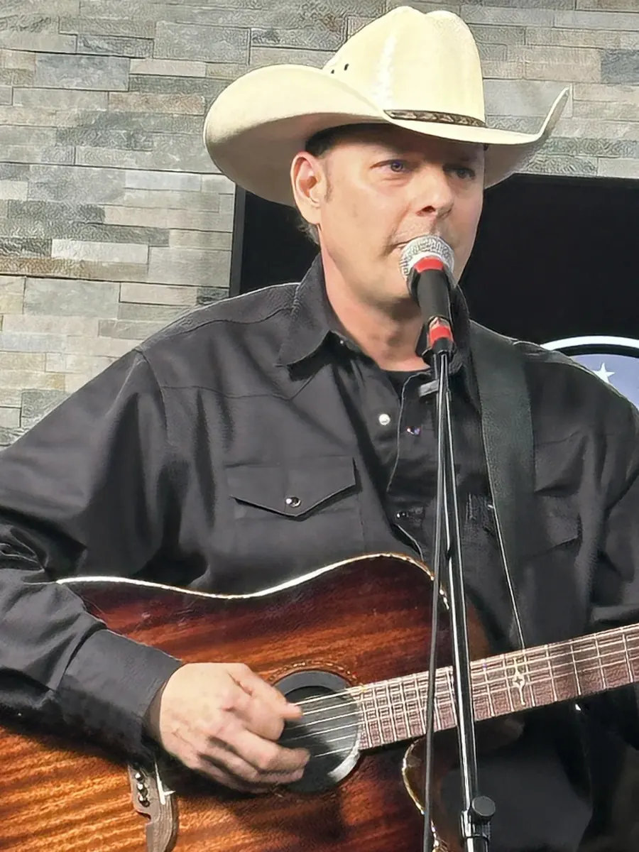Country artist Fred Winston singing and playing acoustic guitar in his cowboy hat