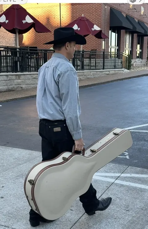 Fred Winston carrying his guitar case down the street